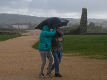 Dos personas se protegen de la lluvia con un paraguas, en la playa de A Lanzada en O Grove, Pontevedra