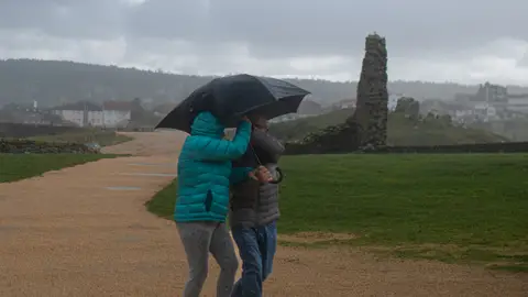 Dos personas se protegen de la lluvia con un paraguas, en la playa de A Lanzada en O Grove, Pontevedra
