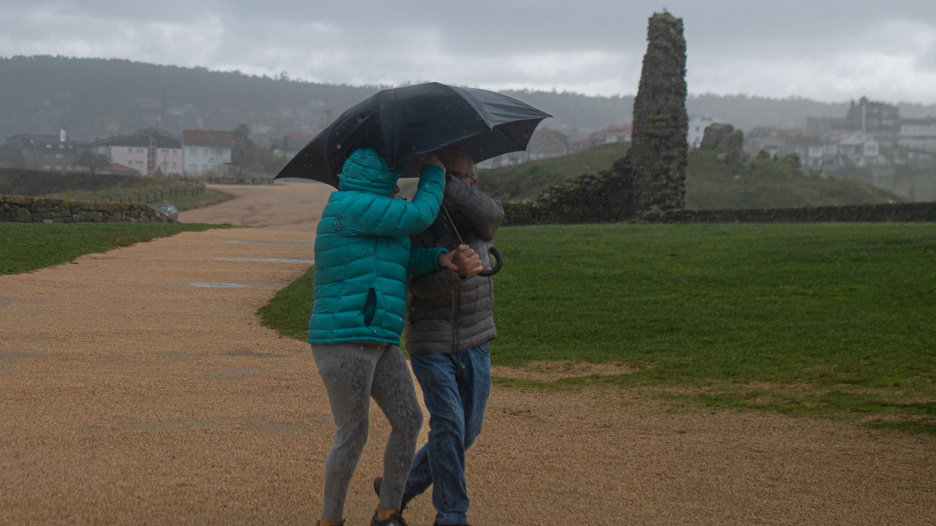 Dos personas se protegen de la lluvia con un paraguas, en la playa de A Lanzada en O Grove, Pontevedra