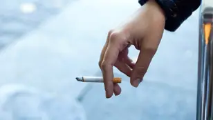 Imagen de la mano de una mujer con un cigarrillo en la calle