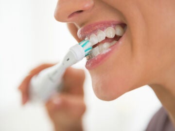 Una mujer se cepilla los dientes con un cepillo eléctrico.