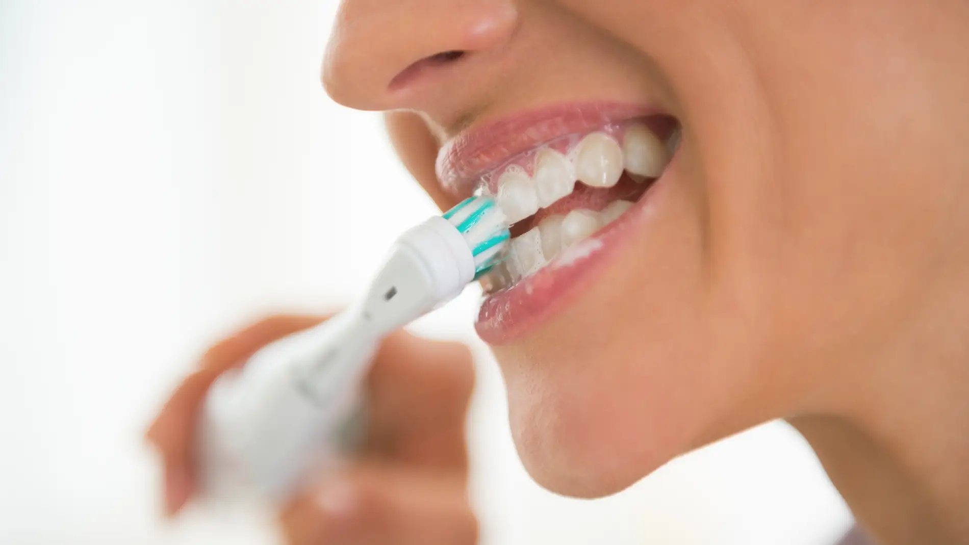 Una mujer se cepilla los dientes con un cepillo eléctrico.