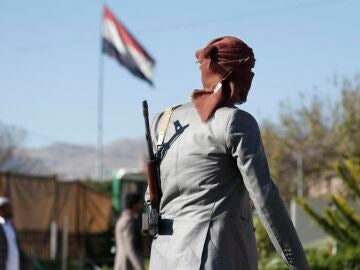 Un combatiente hutí armado pasa junto a una bandera yemení