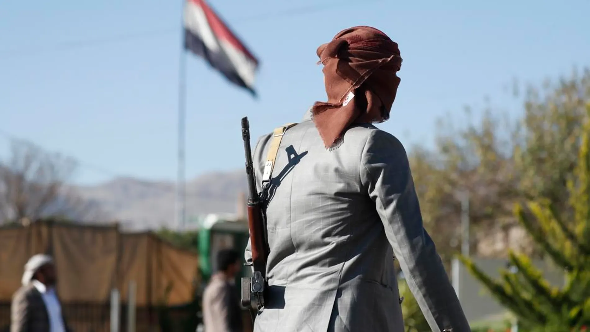 Un combatiente hutí armado pasa junto a una bandera yemení