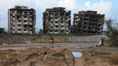 Un gazatí pasa en bici por delante de tres edificios destruidos en Ciudad de Gaza