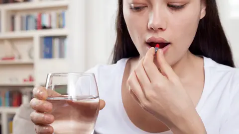 Una mujer a punto de tragarse un medicamento en cápsula Una mujer a punto de tragarse un medicamento en cápsula