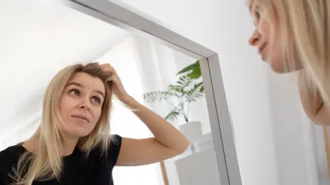 Mujer mirándose el cabello en el espejo Mujer mirándose el cabello en el espejo