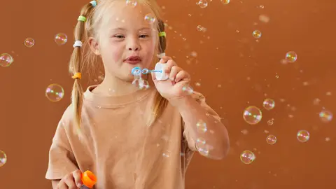 Niña con síndrome de down soplando burbujas Niña con síndrome de down soplando burbujas