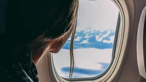 Mujer mirando por la ventanilla de un avión Mujer mirando por la ventanilla de un avión
