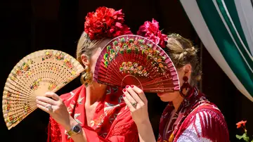 Dos mujeres vestidas de flamenca se protegen del sol 