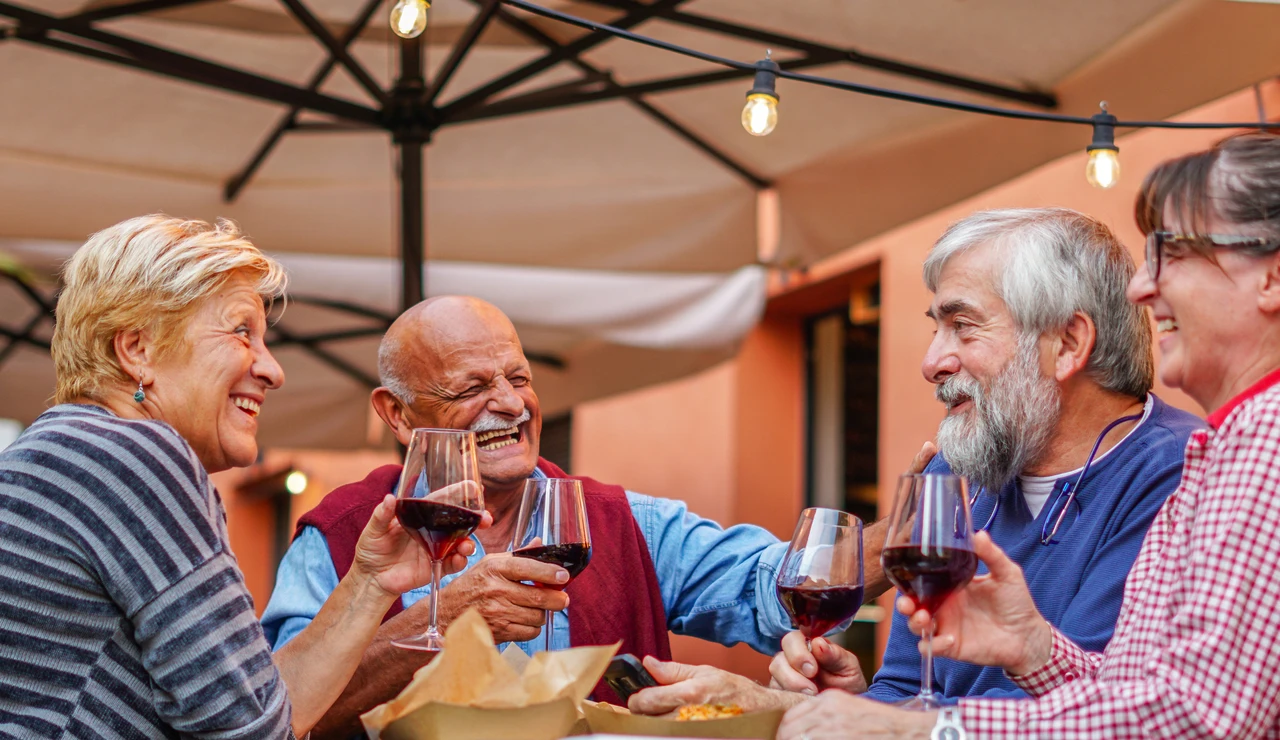 Grupo de personas mayores charlando y riendo mientras beben vino