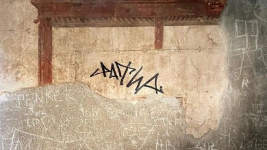 Un turista firma con permanente un fresco de hace siglos en la antigua ciudad de Herculano, Italia
