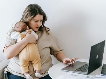 Una mujer trabajando en el ordenador con su bebé en brazos