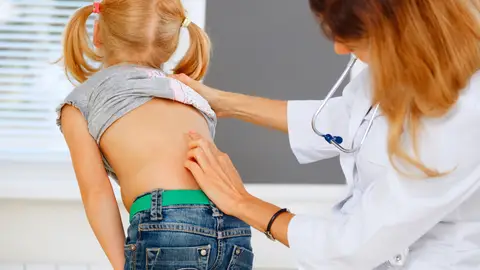 Médico tocando la columna vertebral a una niña Médico tocando la columna vertebral a una niña