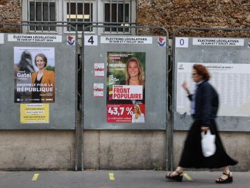 Una mujer pasa junto a un cartel de los candidatos del Nouveau Front Populaire para las elecciones parlamentarias en París