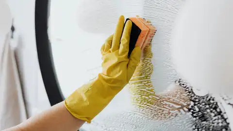 Persona limpìando un espejo con un estropajo Persona limpiando un espejo con un estropajo