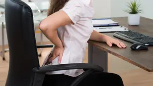 Una persona con dolor de espalda al sentarse mal