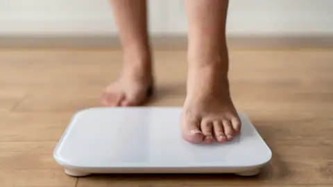 Persona pesándose en una báscula Persona pesándose en una báscula