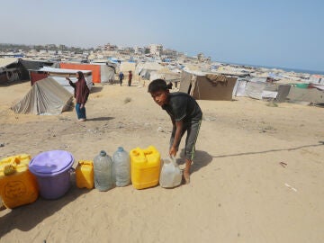 Un niño palestino junto a varios bidones cerca de un punto de recogida de agua en Al Zauaida, en el centro de la Franja de Gaza