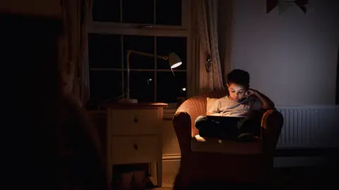 Un niño leyendo a oscuras con un flexo Un niño leyendo a oscuras con un flexo