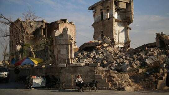 Un vendedor ambulante se sienta el 5 de diciembre de 2024 frente a un edificio da&ntilde;ado en Siria