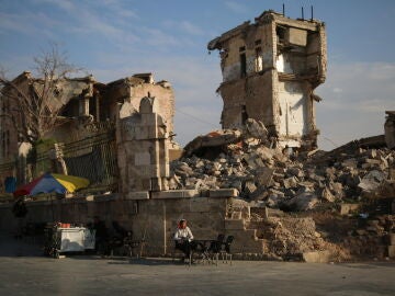 Un vendedor ambulante se sienta el 5 de diciembre de 2024 frente a un edificio dañado en Siria