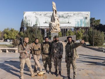 Miembros de grupos armados insurgentes posan tras el derribo de una estatua del expresidente Hafez al Assad