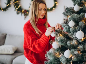 Mujer decorando el árbol de Navidad con un jersey rojo Mujer decorando el árbol de Navidad con un jersey rojo