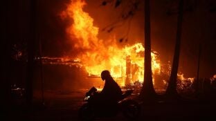 Una persona conduce su motocicleta junto a una casa en llamas durante los incendios en California