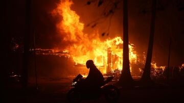 Una persona conduce su motocicleta junto a una casa en llamas durante los incendios en California