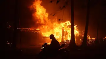 Una persona conduce su motocicleta junto a una casa en llamas durante los incendios en California Una persona conduce su motocicleta junto a una casa en llamas durante los incendios en California