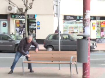 Hombre sujetándose a un banco por el viento