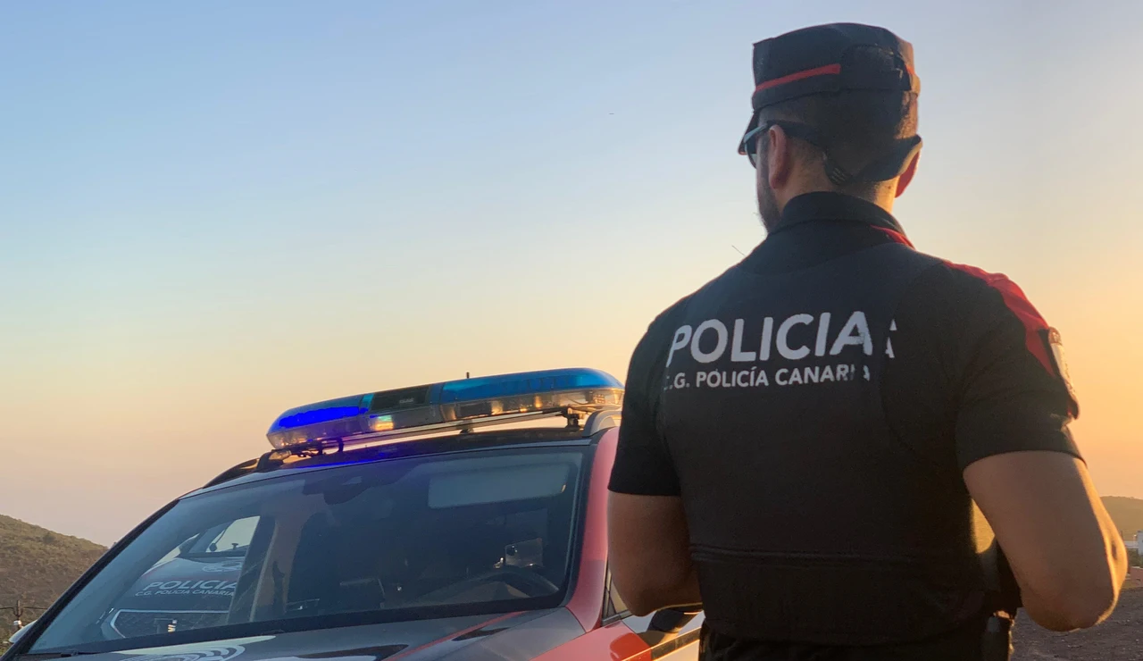 Agente de la Policía Canaria junto a un coche patrulla.