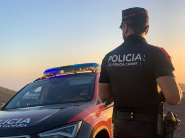 Agente de la Policía Canaria junto a un coche patrulla.