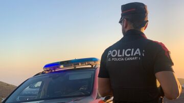 Agente de la Policía Canaria junto a un coche patrulla.