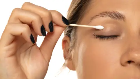 Mujer limpiando la máscara de pestañas con un bastoncillo Mujer limpiando la máscara de pestañas con un bastoncillo
