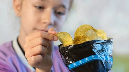 Una niña cogiendo una patata frita de la bolsa Una niña cogiendo una patata frita de la bolsa