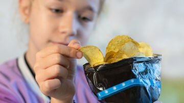 Una niña cogiendo una patata frita de la bolsa 