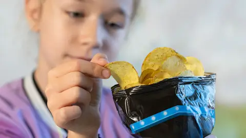 Una niña cogiendo una patata frita de la bolsa  Una niña cogiendo una patata frita de la bolsa