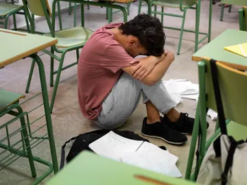 Un adolescente en el suelo de la clase con la cara tapada Un adolescente en el suelo de la clase con la cara tapada