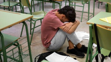 Un adolescente en el suelo de la clase con la cara tapada