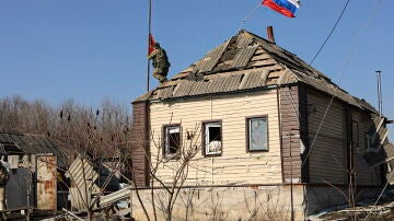 Un soldado ruso instalando una bandera roja en el techo de un edificio privado dañado en un pueblo de la región de Kursk