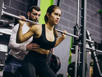Una mujer realiza ejercicio con pesas junto a un entrenador personal Una mujer realiza ejercicio con pesas junto a un entrenador personal