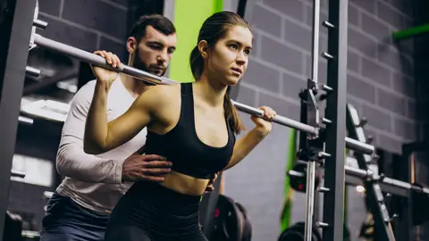 Una mujer realiza ejercicio con pesas junto a un entrenador personal Una mujer realiza ejercicio con pesas junto a un entrenador personal
