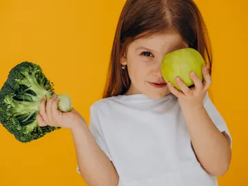 Una niña con un brócoli y una manzana Una niña con un brócoli y una manzana