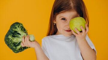 Una niña con un brócoli y una manzana