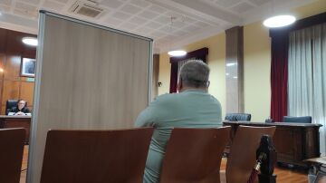 El acusado, sentado en el banquillo y separado por un biombo, escucha la declaración de su exmujer