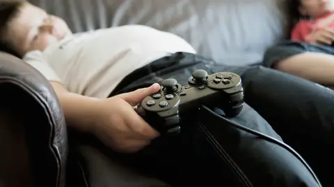 Niños con obesidad dormidos en el sofá con el mando de los videojuegos Niños con obesidad dormidos en el sofá con el mando de los videojuegos