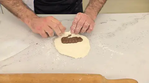 Forma un bollo alargado, envolviendo la crema de cacao con la masa Forma un bollo alargado, envolviendo la crema de cacao con la masa