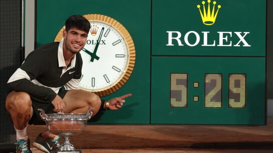 Alcaraz posa con la Copa de los Mosqueteros junto al reloj que marca el tiempo que dur&oacute; la final de Roland Garros